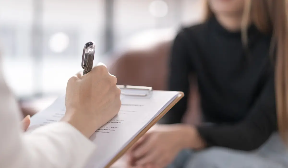 Close-up of a counselor writing notes on a clipboard while meeting with a teenager, illustrating rehabilitation support for minors after Juvenile Arrests in Naperville.