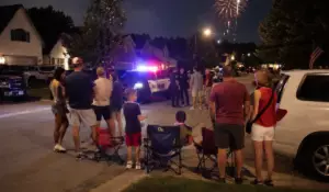 Neighborhood Fourth of July celebration with fireworks overhead and police officers responding to an incident, illustrating Independence Day Arrests and holiday-related criminal investigations in Illinois.
